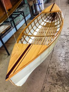 The Lotus 2 Skin on Frame Canoe boat for sale built by Bayou Boats hanging on strings in a warehouse
